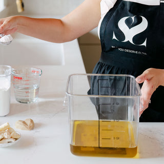 Founder of Blissed Botanical Co in the kitchen with a large measuring tub mixing organic extra virgin olive oil making cold process soaps