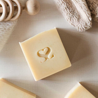 Overhead image of cold process soap on a linen sheet with wooden and plush baby toys