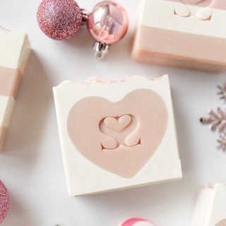 Pink peppermint soap with a heart in the middle sitting on a marble countertop with pink christmas ornaments
