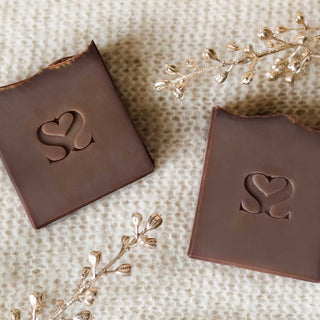 Two Cozy Cocoa Butter Cashmere cold process soap bars on a cashmere blanket with gold sparkle decor