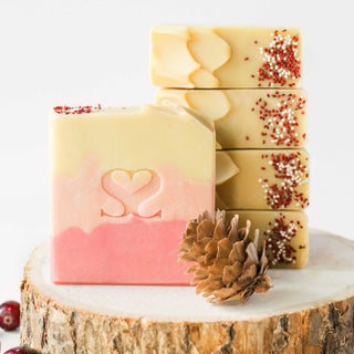 Larger than life image of Crackling Cranberry cold process soap on top of a wooded tree trunk with pinecones and cranberries resting next to them